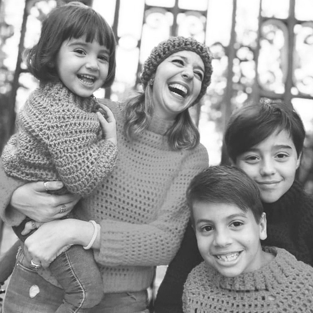 Julieta Campelli riendo junto a sus tres hijos, todos con prendas tejidas
