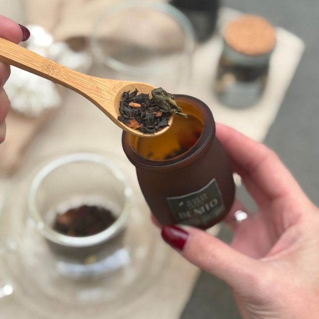 Manos sirviendo hebras de té con una cuchara de madera